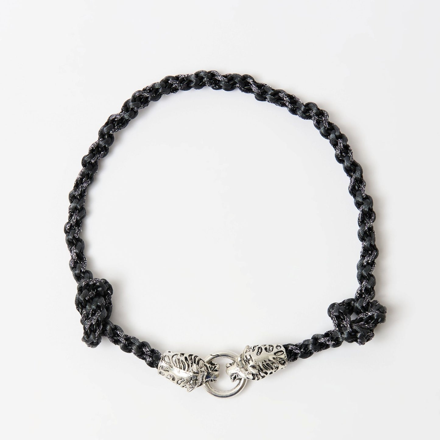 Top-down view of a black braided necklace with a silver tiger head clasp and knot detailing on each side.