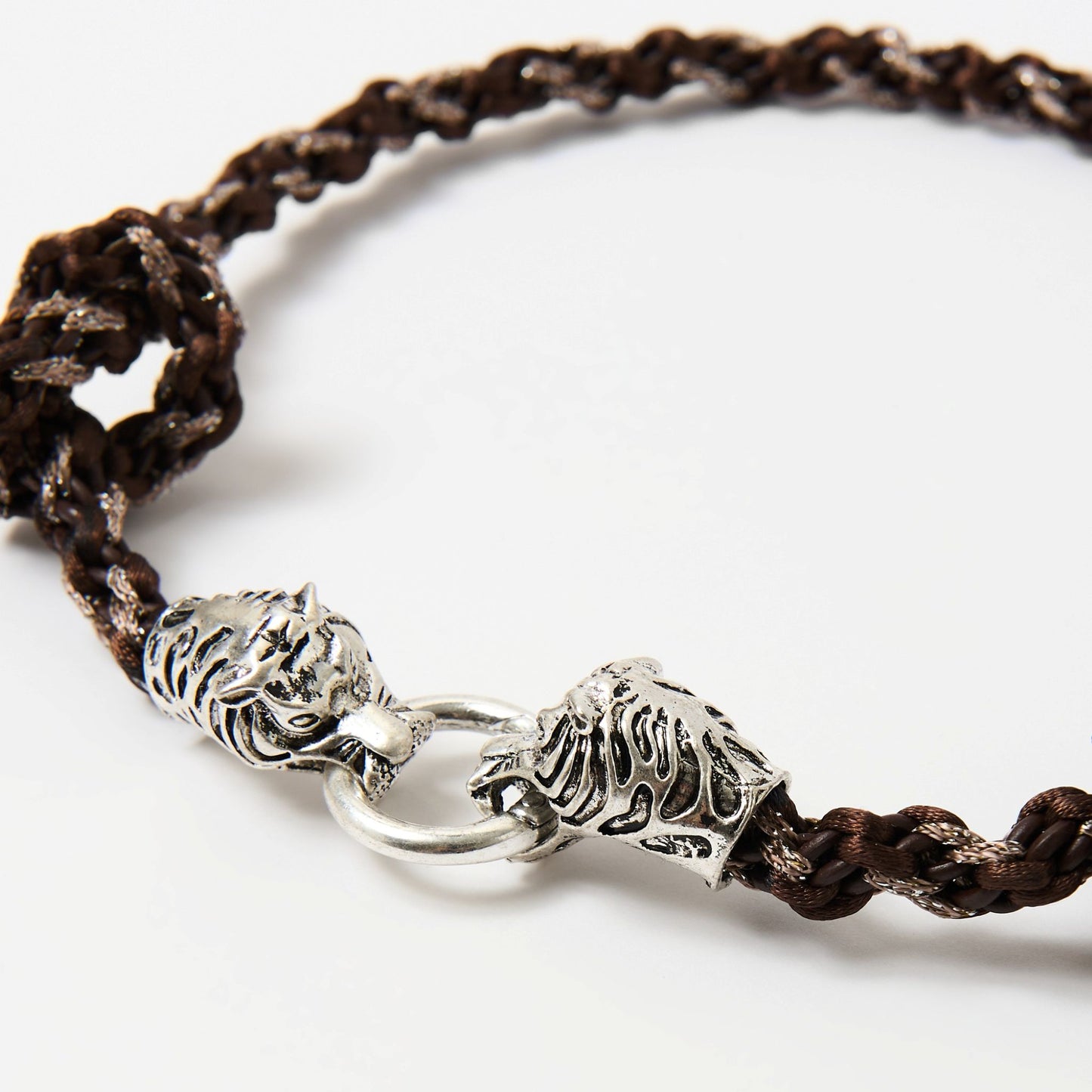 Close-up of a braided cord necklace in dark brown tones featuring a silver tiger head clasp with intricate detailing, each head gripping a central metal ring.