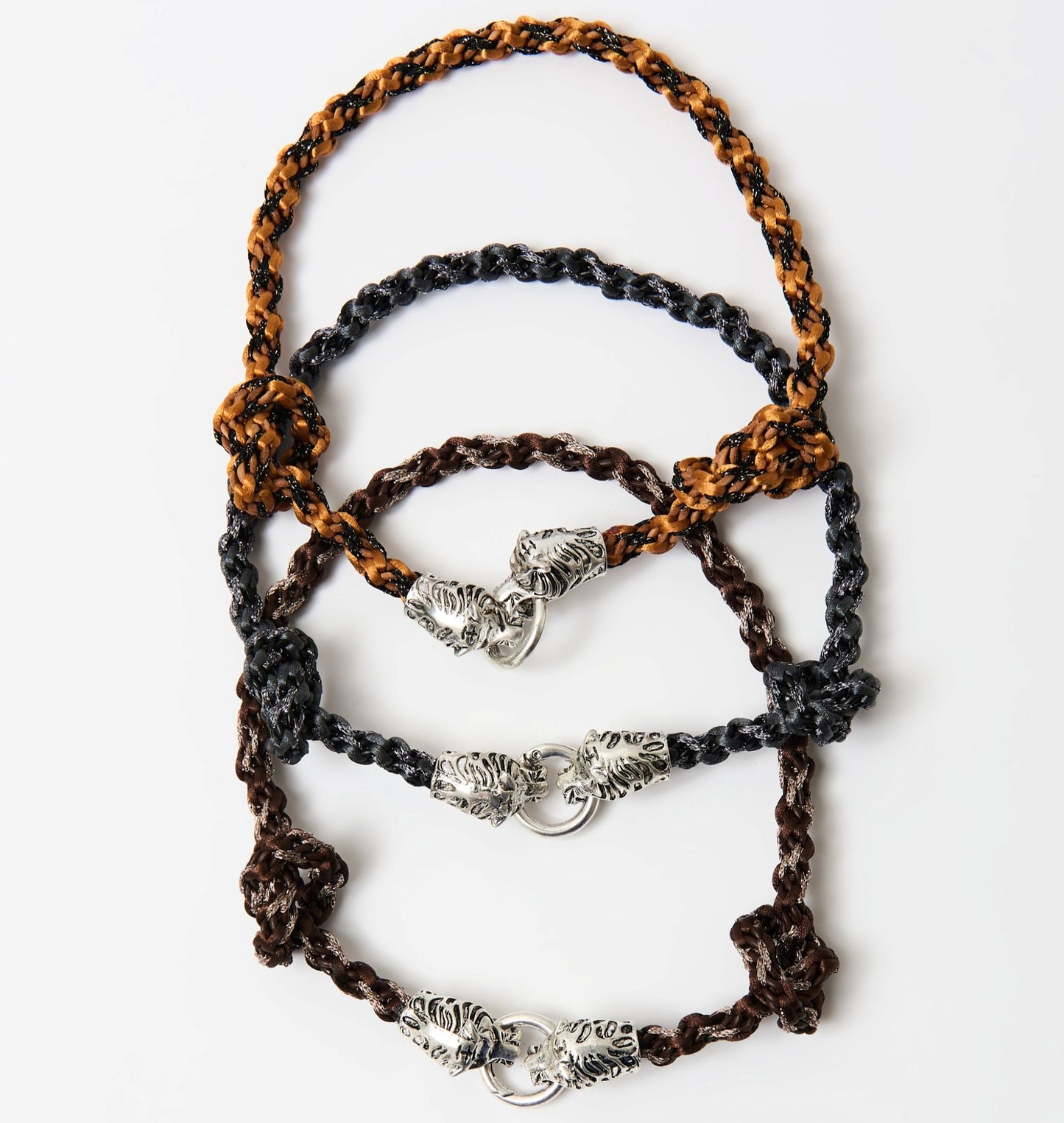 Three braided cord necklaces in black, brown, and orange-black combinations, each with a silver tiger head clasp, arranged in a layered arc.