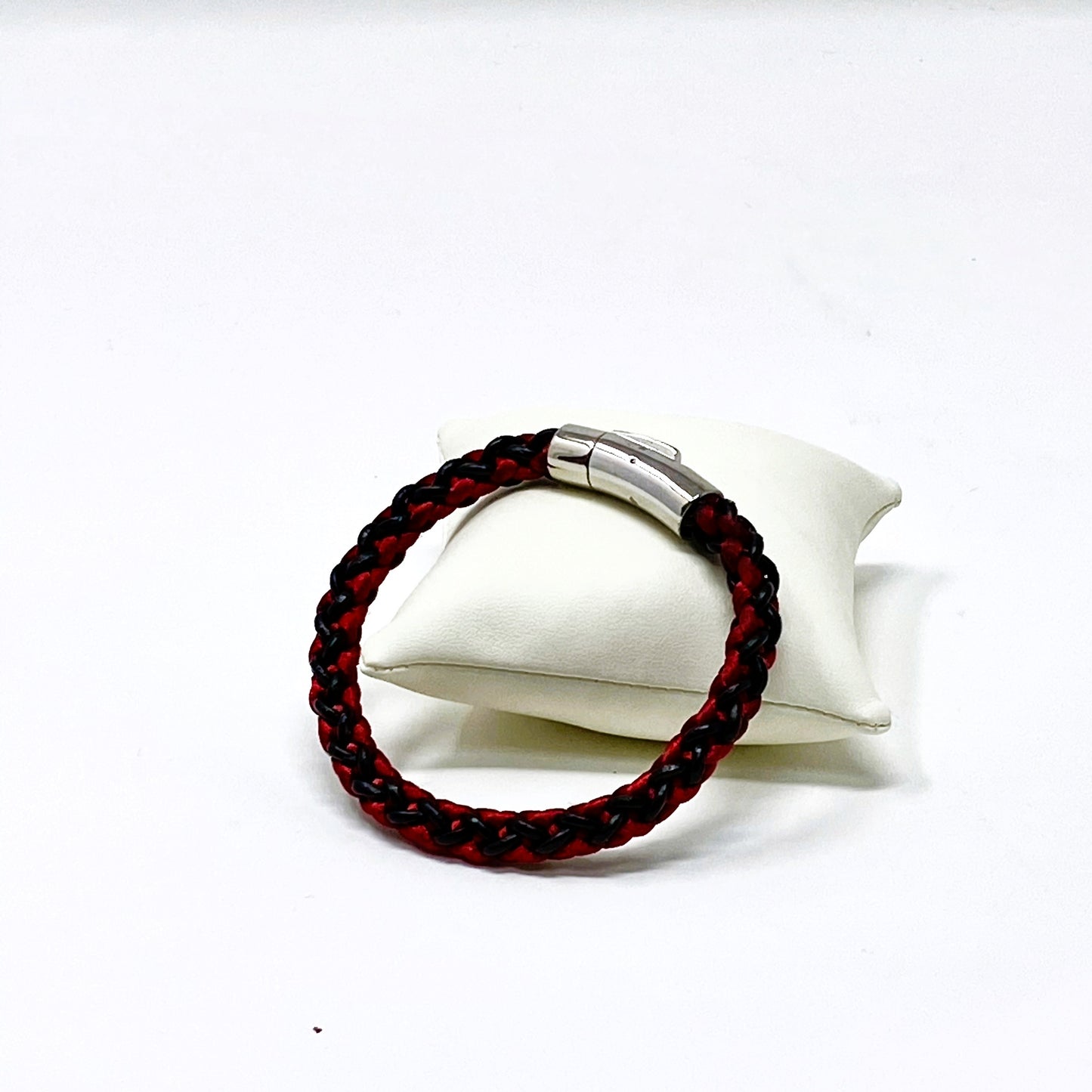 Red and black braided bracelet with silver clasp on a white stand against a white background