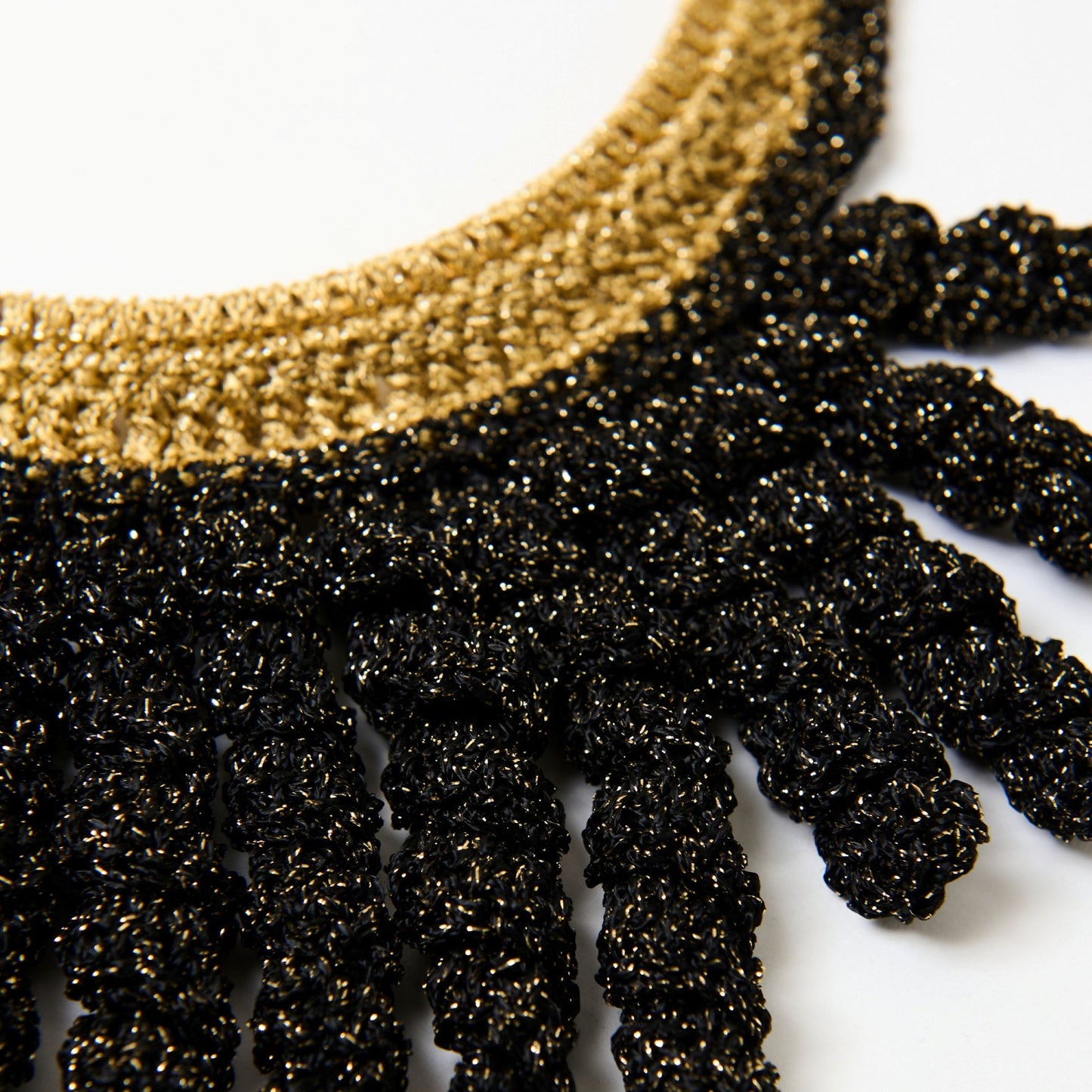 Detailed close-up of a handmade statement necklace featuring a gold neckline and black frilled spiral fringe, with a shimmering metallic finish.
