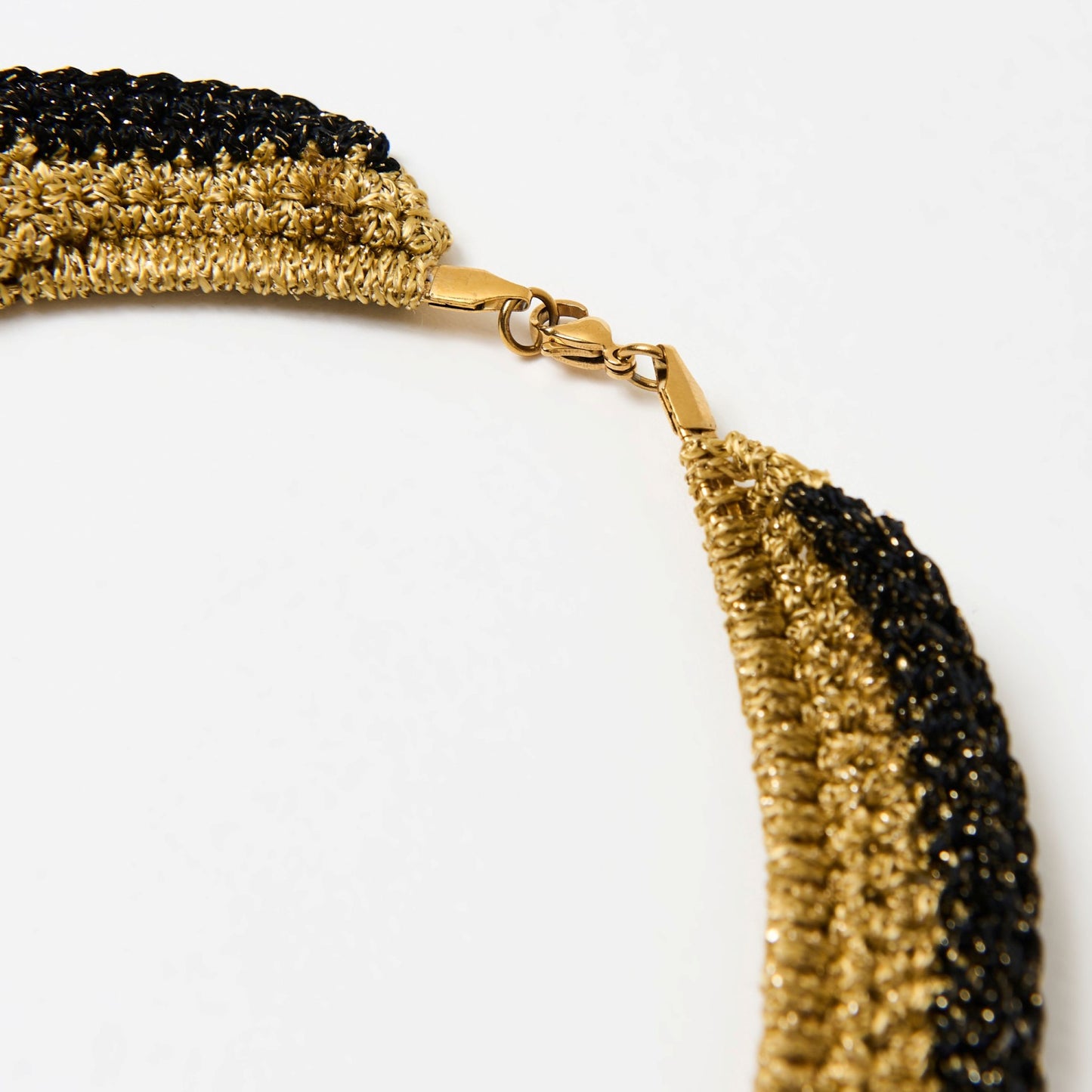 Detailed view of the lobster clasp fastening on a metallic gold and black handmade statement necklace.