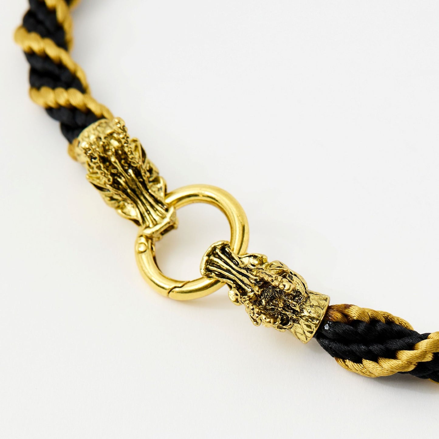 Side close-up of detailed gold-tone dragon head clasp securing a black and gold satin rope necklace.
