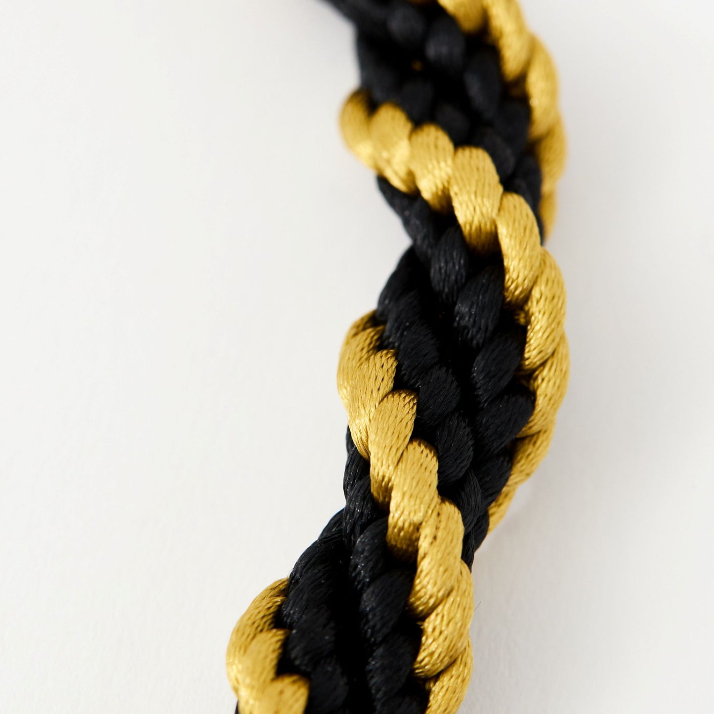 Macro close-up of twisted black and gold satin cord, highlighting the silky braided texture and bold contrast.