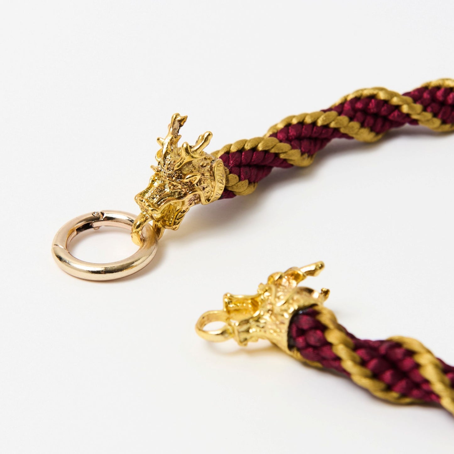 Close-up of gold-tone dragon head clasp open at the ring, showing detailed texture and red-gold cord braid.