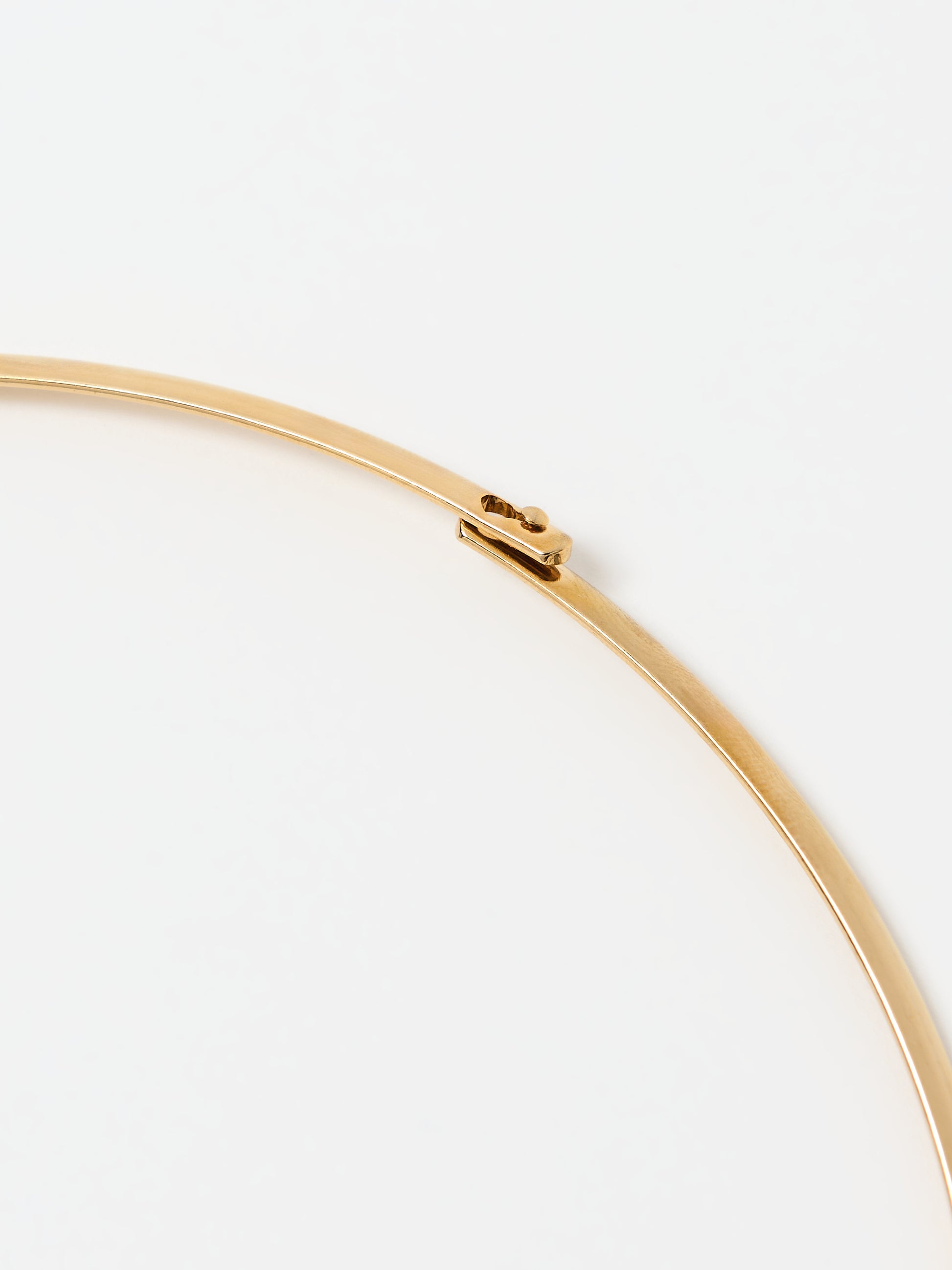 A close-up of the clasp mechanism of a gold choker necklace. The sleek, minimalist design of the clasp blends seamlessly with the smooth gold finish, showcasing precision craftsmanship and understated elegance.