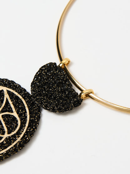 A detailed close-up of the gold choker necklace focusing on the connection between the choker and the black textured pendant. The intricate black design with subtle gold accents attaches to the sleek gold frame with precision, highlighting the craftsmanship and elegant aesthetic of the jewelry.