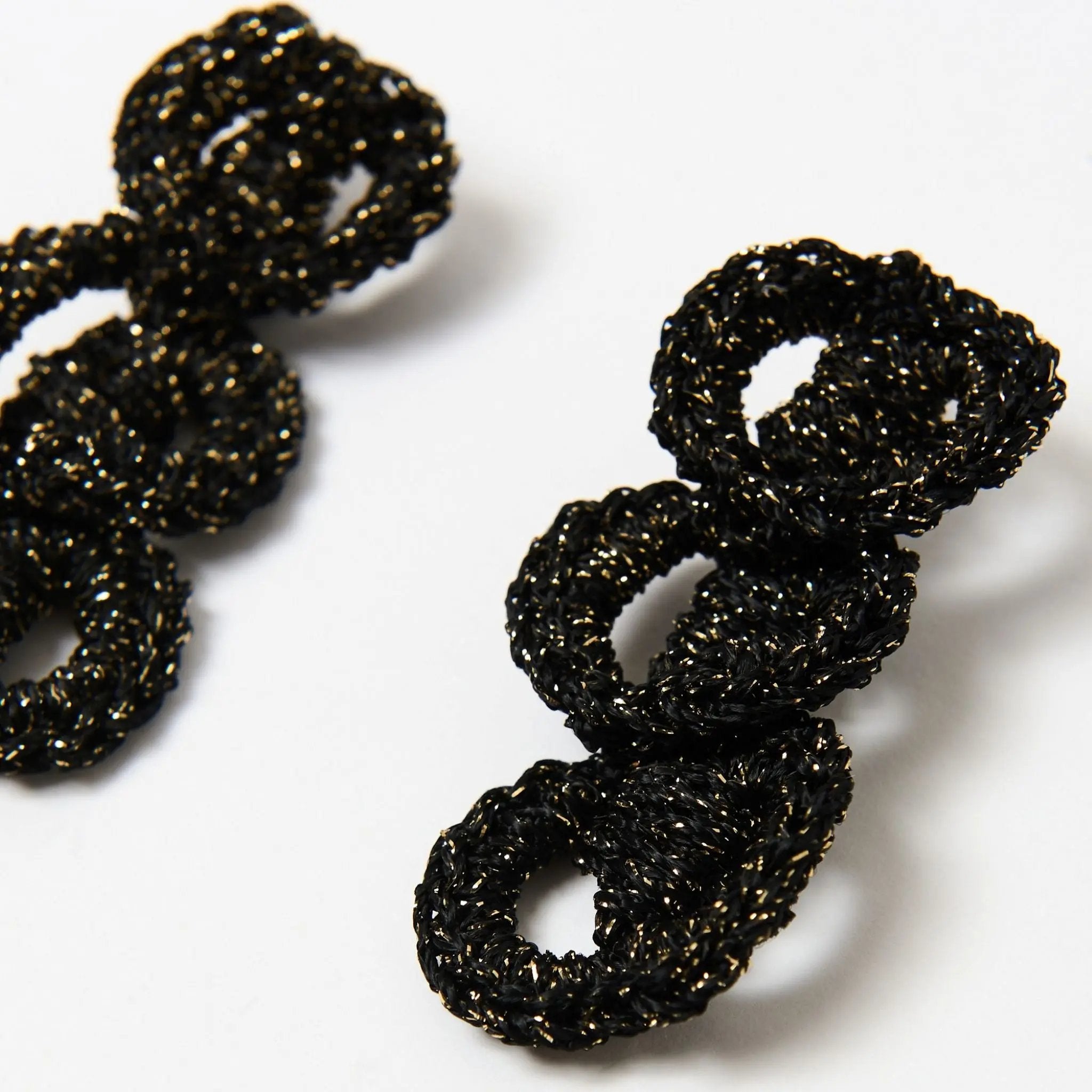 Close-up of hand-crocheted black and gold loop earrings featuring a shimmering twisted yarn and bold sculptural shape.