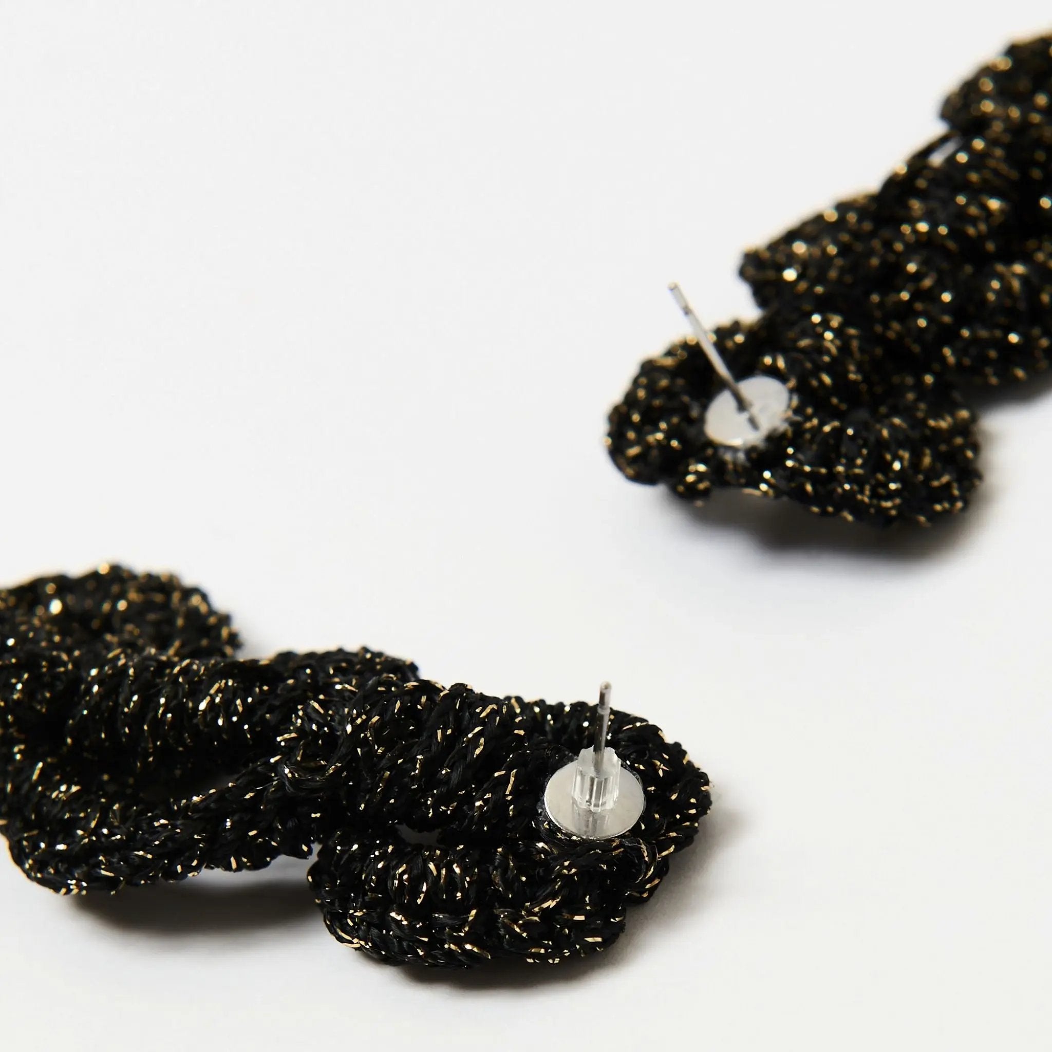 Detail of black and gold statement earrings showing stainless steel post with clear silicone back.