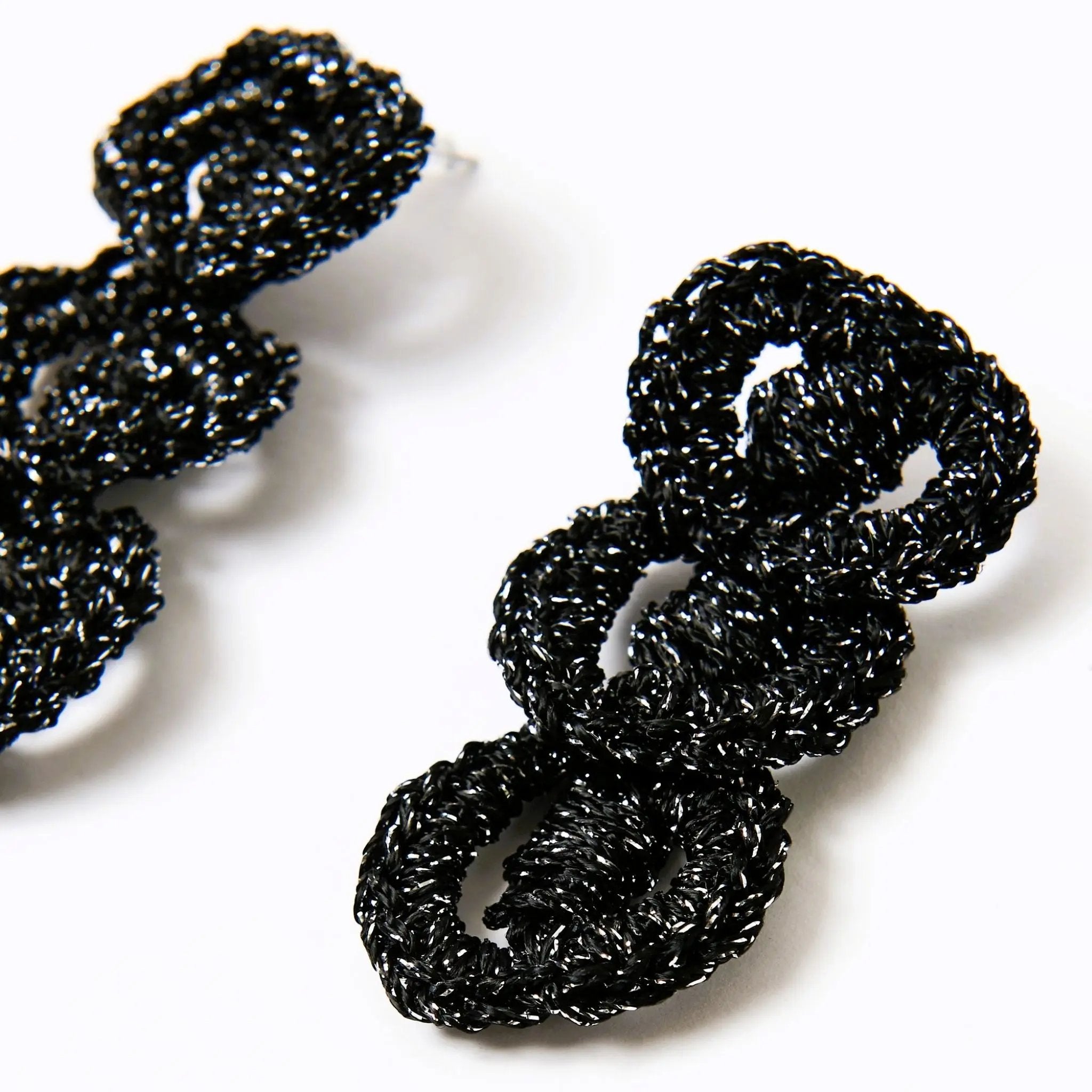 Close-up of handmade black and silver loop earrings, highlighting their linked circular design and glimmering texture.