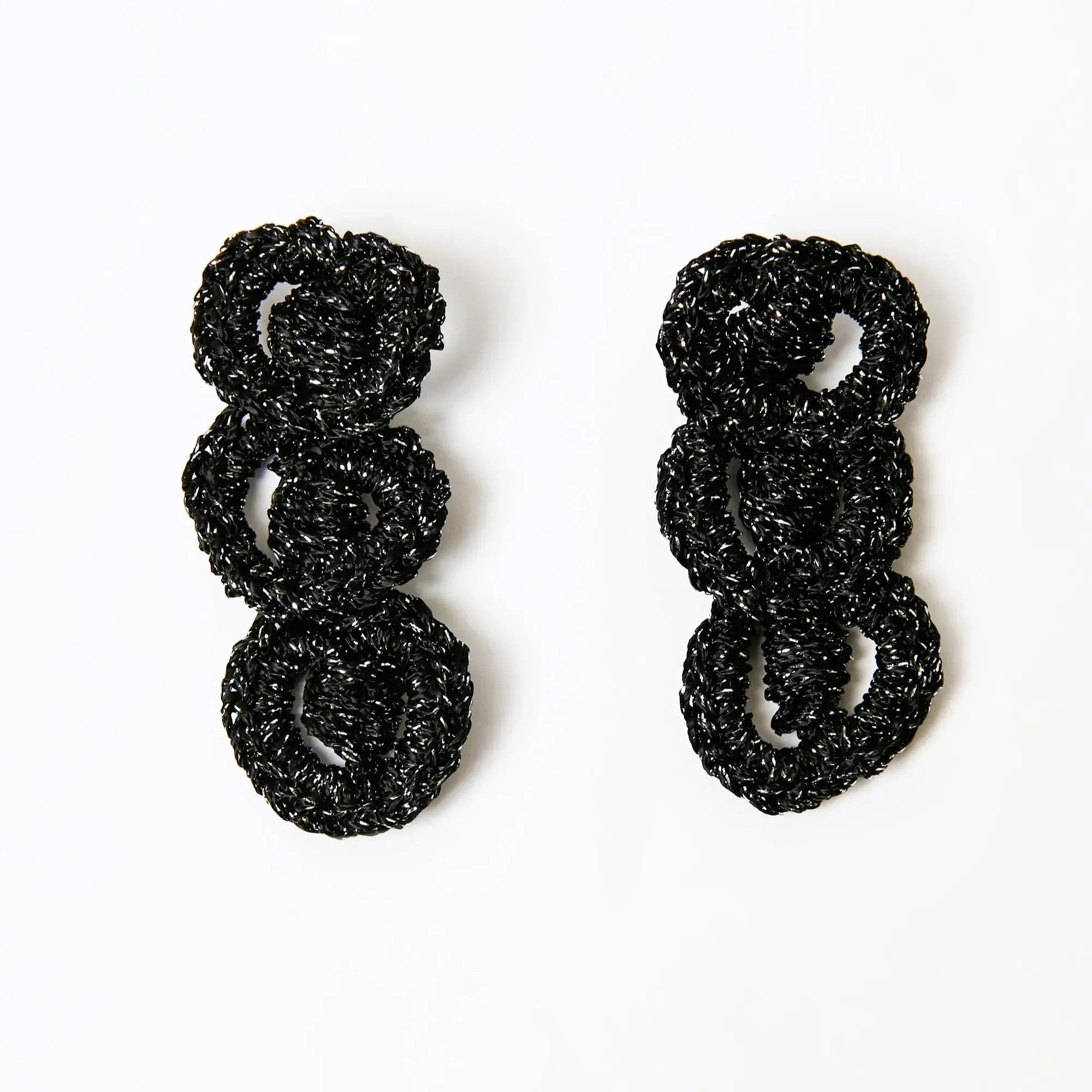 Statement loop earrings in black and silver hand-crocheted yarn, laid flat against a clean white background.