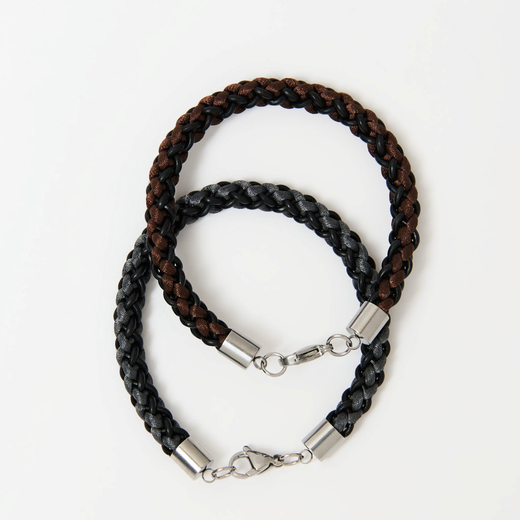 The Marlowe braided leather bracelets in Chestnut Brown and Graphite Grey with silver lobster clasps, laid flat together
