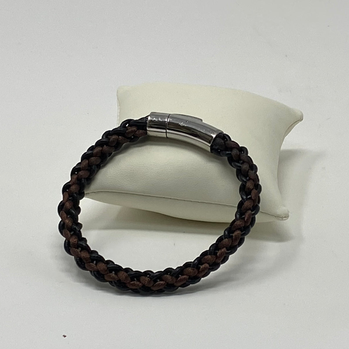 The Arden men's braided leather bracelet in Chestnut Brown displayed on a cushion, polished silver magnetic clasp