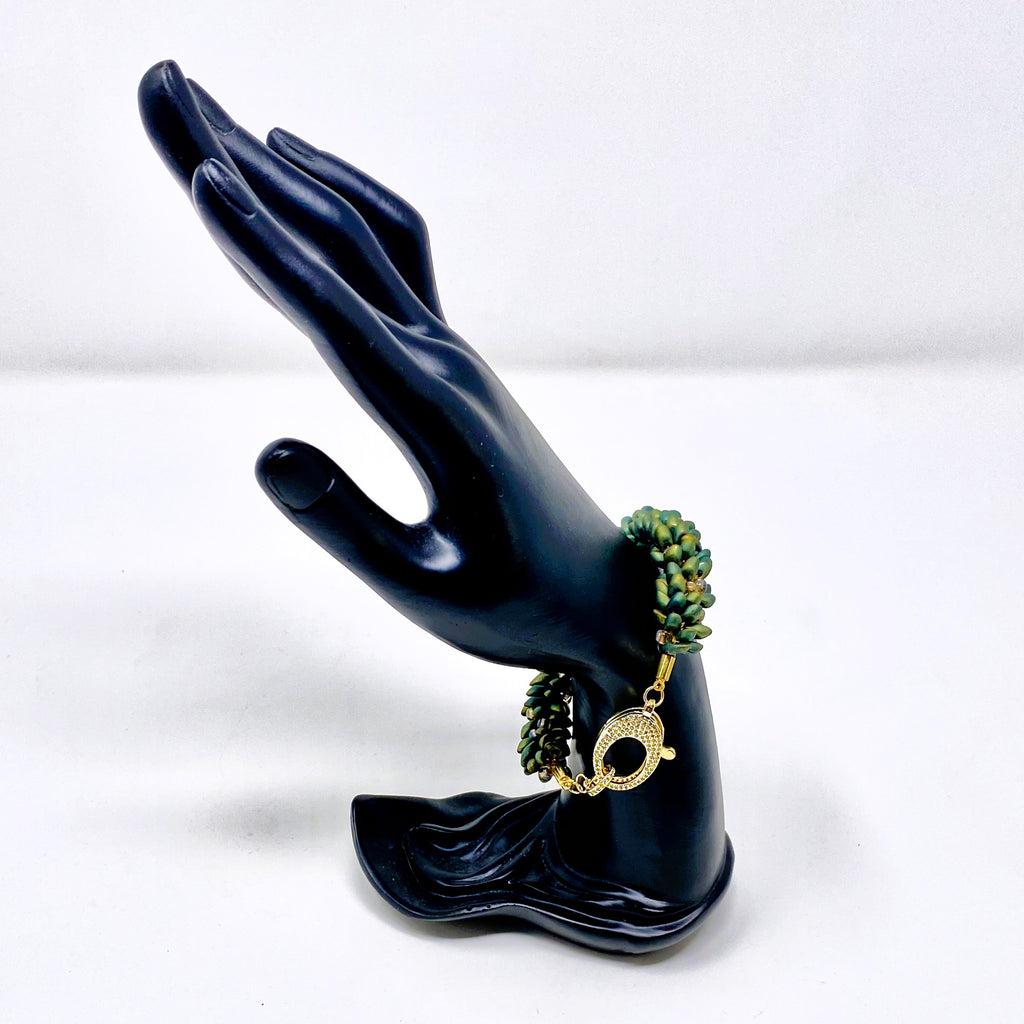The Elio beaded bracelet in green and gold shown on a black hand display