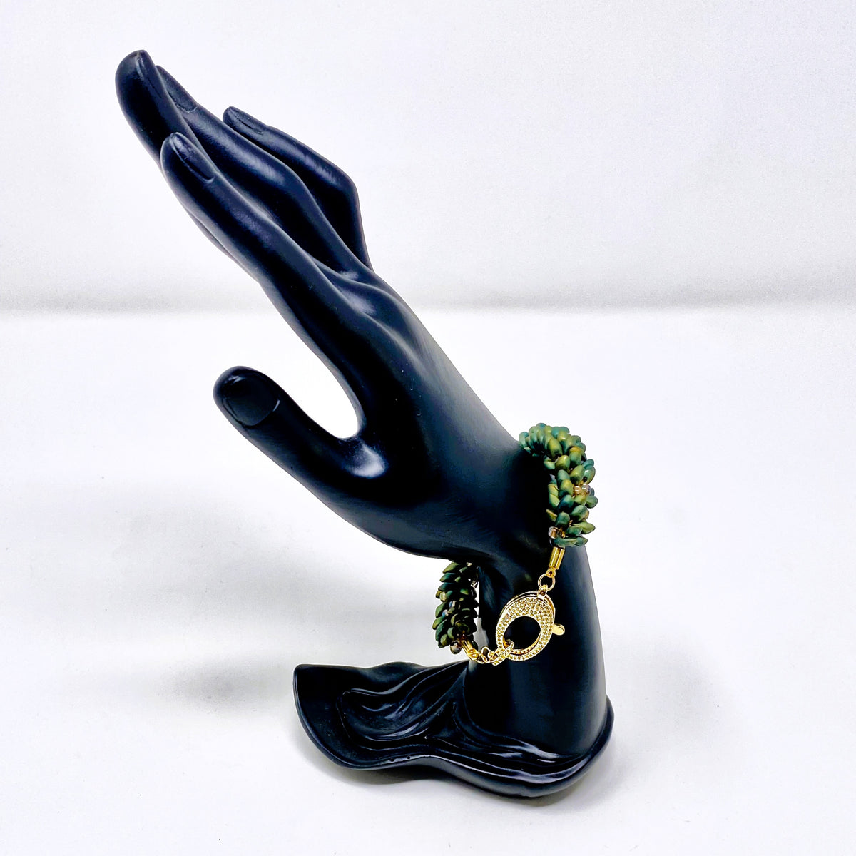 The Elio beaded bracelet in green and gold shown on a black hand display