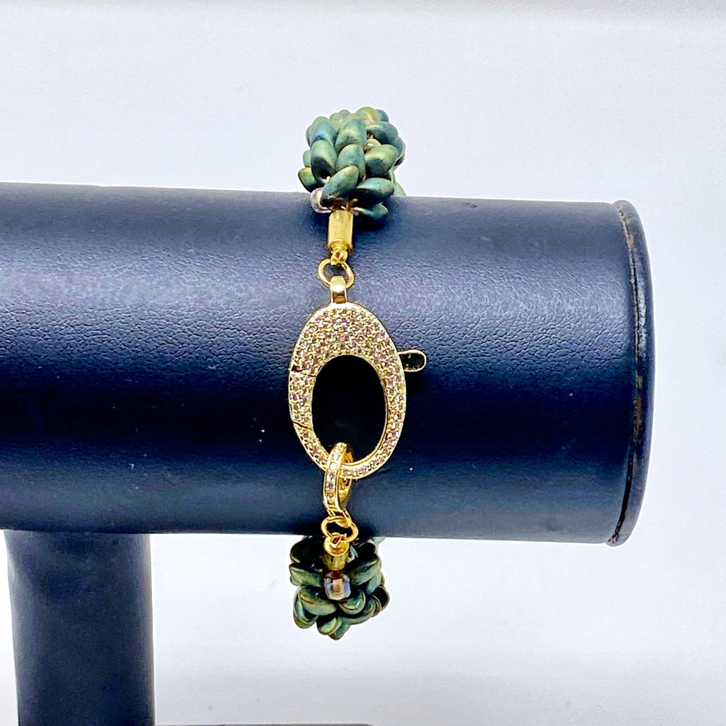 The Elio beaded bracelet in green and gold on a display stand, focus on the crystal-set gold clasp