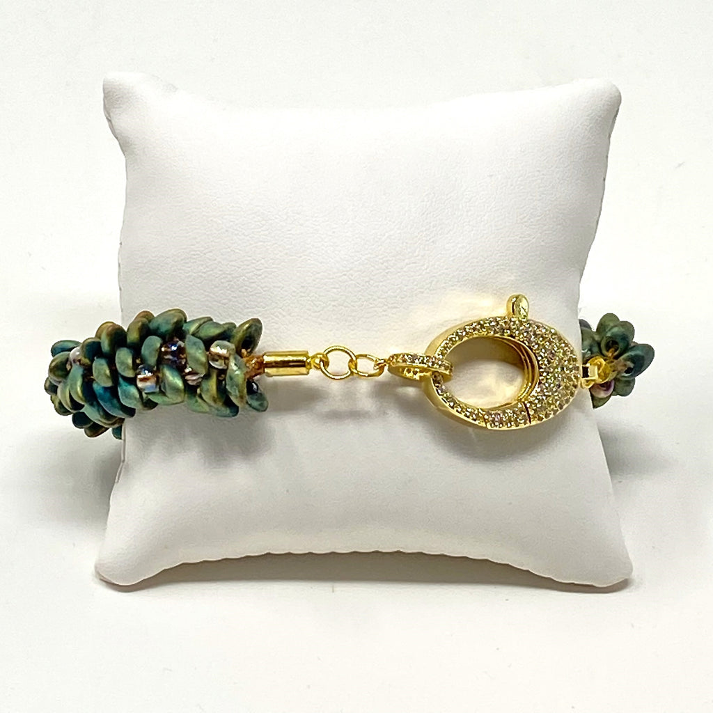 The Elio beaded bracelet in green and gold shown on a white display cushion