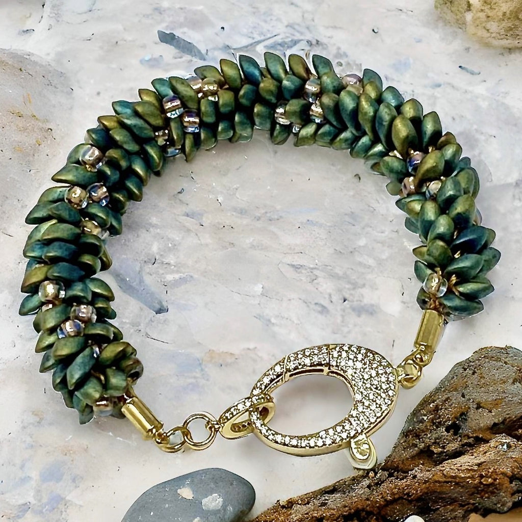 The Elio green and gold beaded bracelet with crystal-set gold clasp, laid on stone and rock
