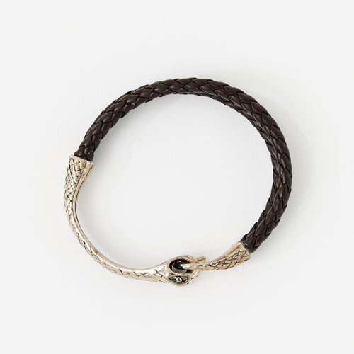 The Serin leather bracelet in Chestnut Brown with a sculptural silver snake clasp, laid flat on white