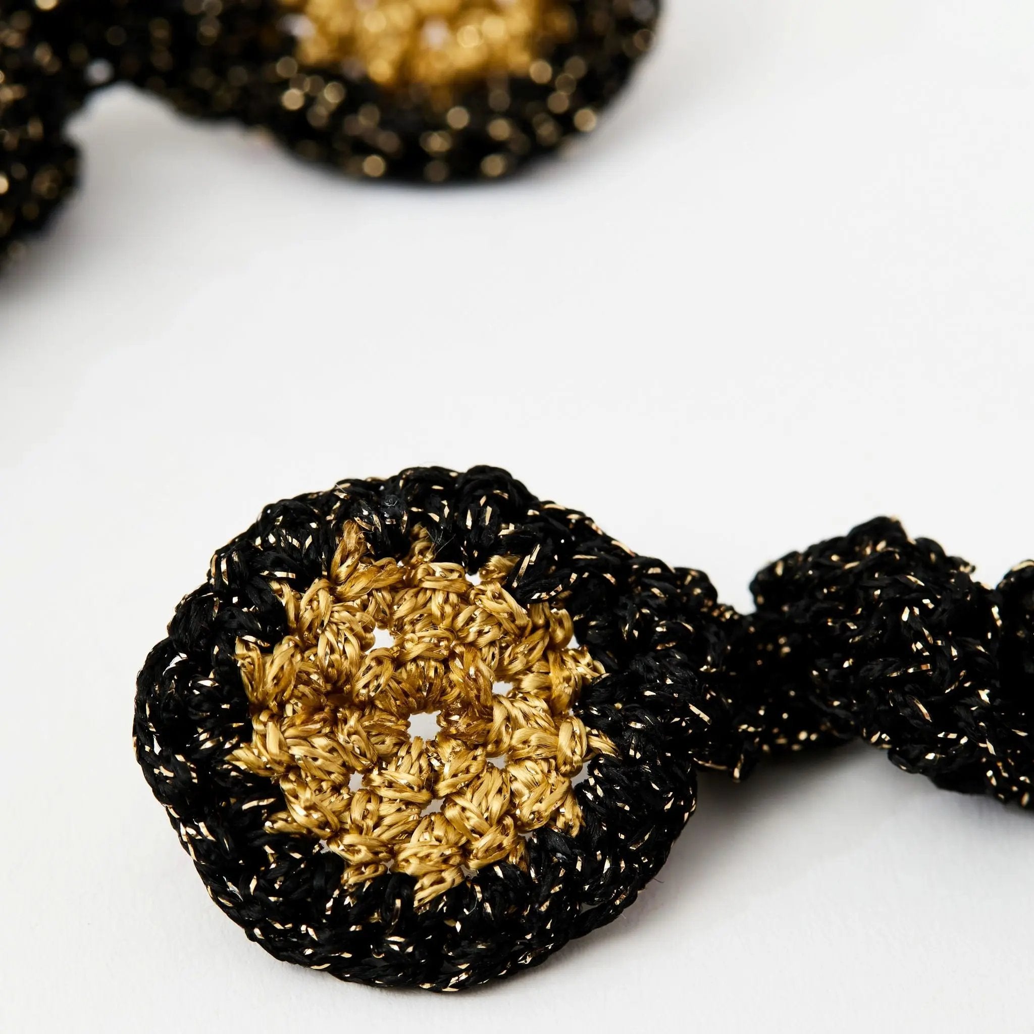 Close-up of gold and black crochet earrings showing the textured sunburst centre and shimmering black edging.