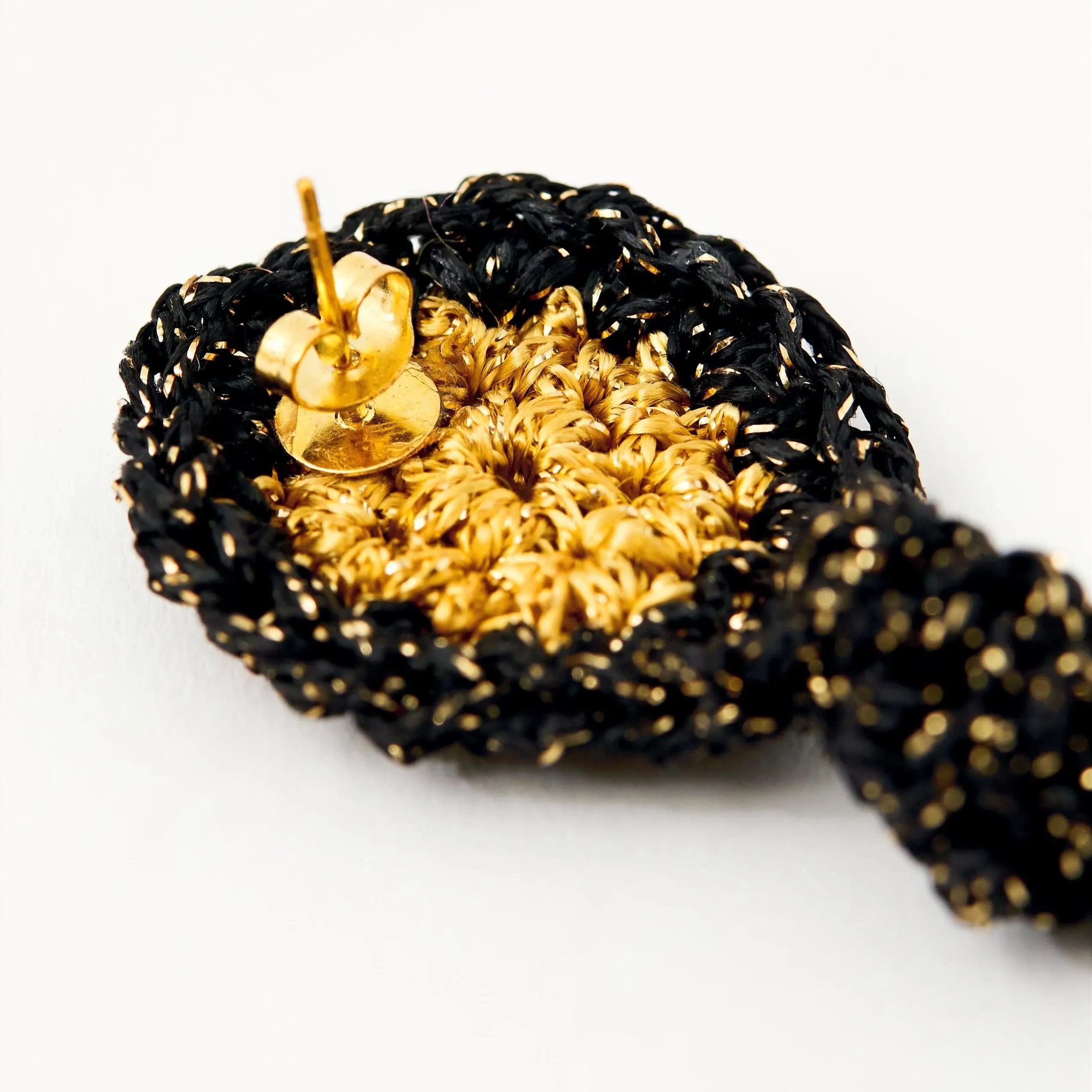 Detail of gold-tone earring post and butterfly backing stitched into a black and gold crocheted disc.