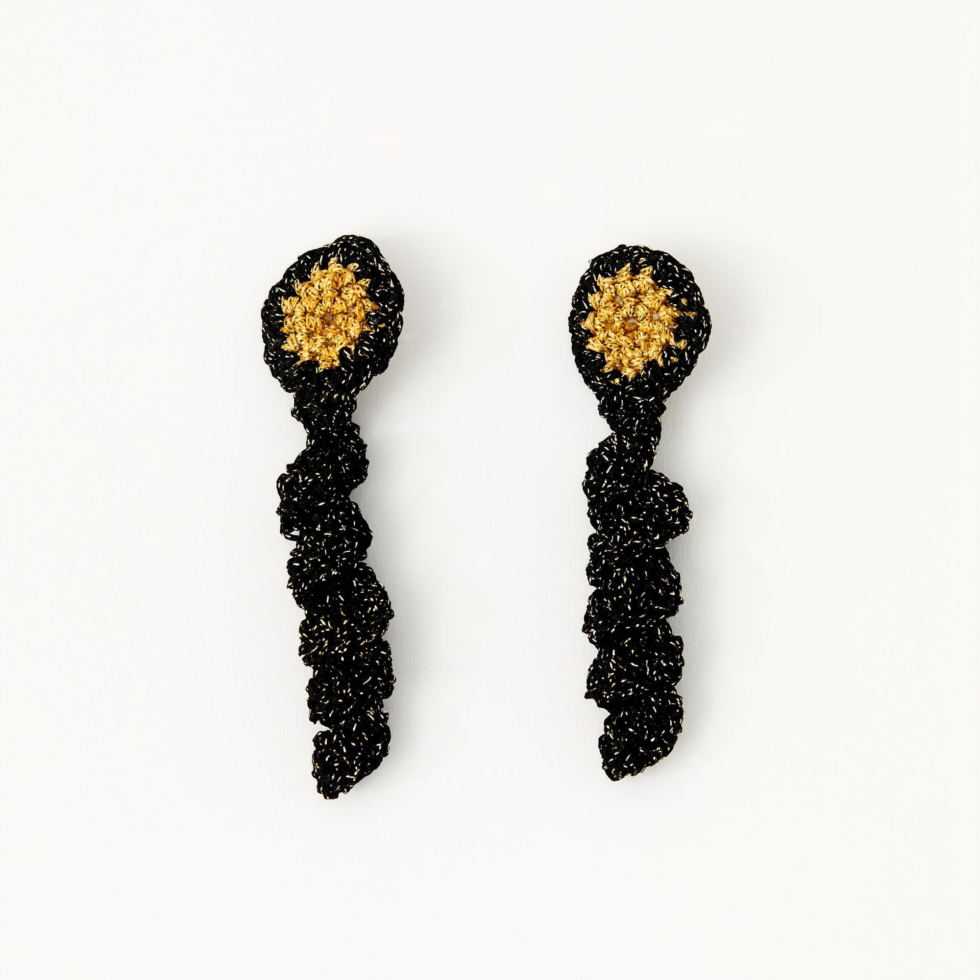 Hand-crocheted disc earrings with golden centre and black frilled drop, laid flat against a white background.