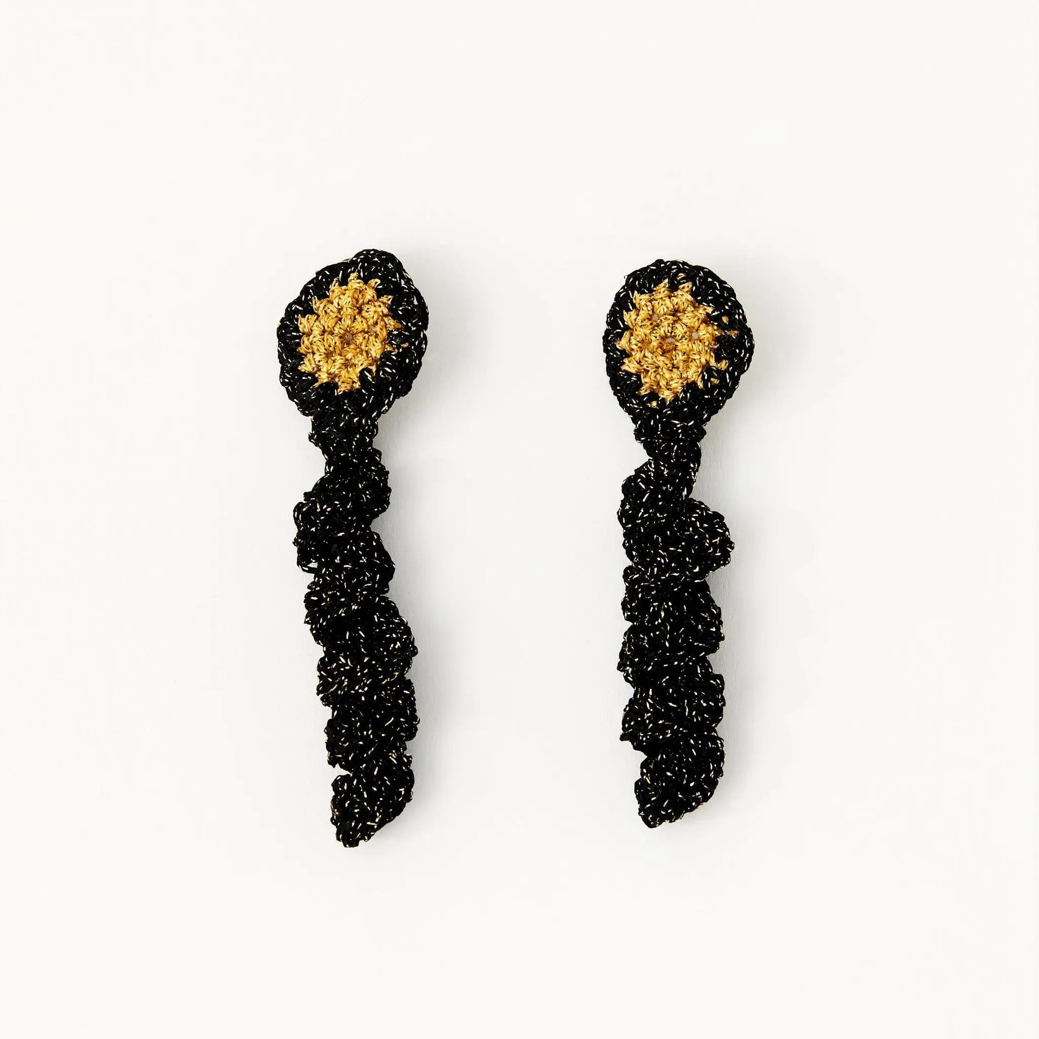 Hand-crocheted disc earrings with golden centre and black frilled drop, laid flat against a white background.