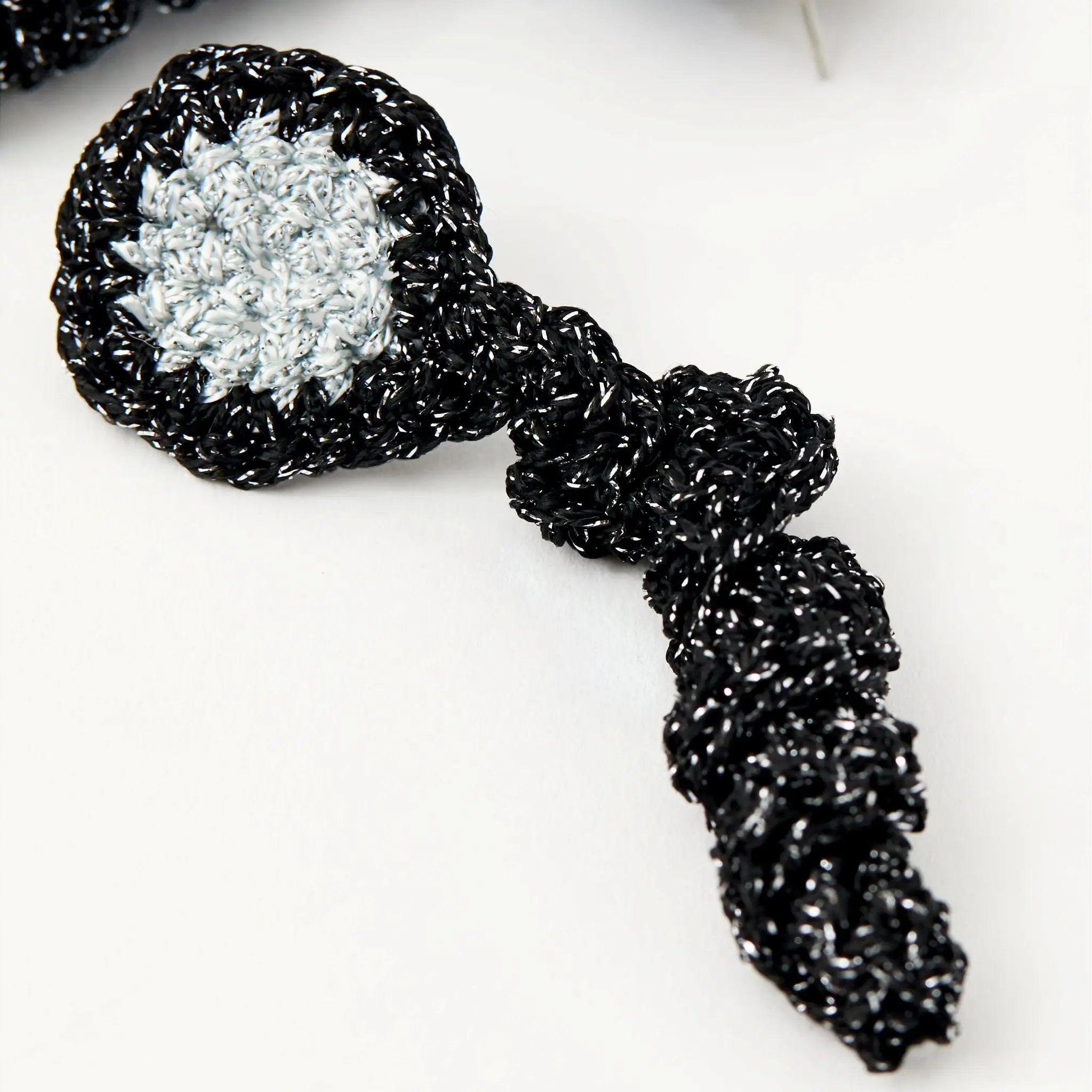 Macro detail of crocheted black spiral drop earring with a silvery hand-stitched centre.