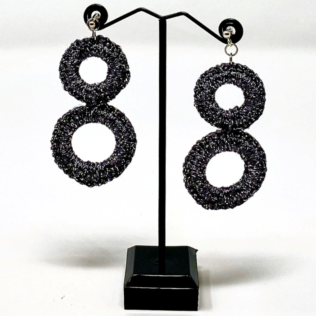 The Sienna charcoal grey crochet double-ring earrings hanging on a black earring stand - Lodorfo