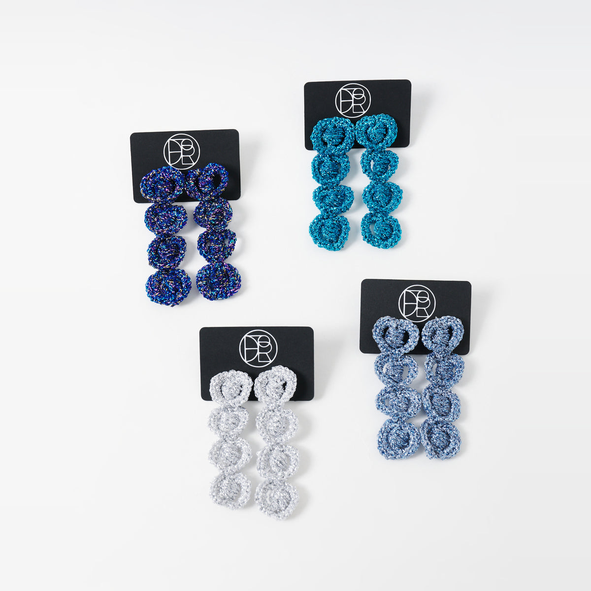 The Arlo long crochet loop earrings in indigo blue, deep teal, silver grey and sky blue on black earring cards - Lodorfo