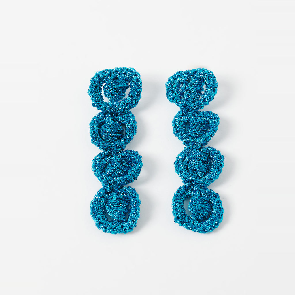 The Arlo long deep teal four-ring crochet loop earrings laid flat - Lodorfo