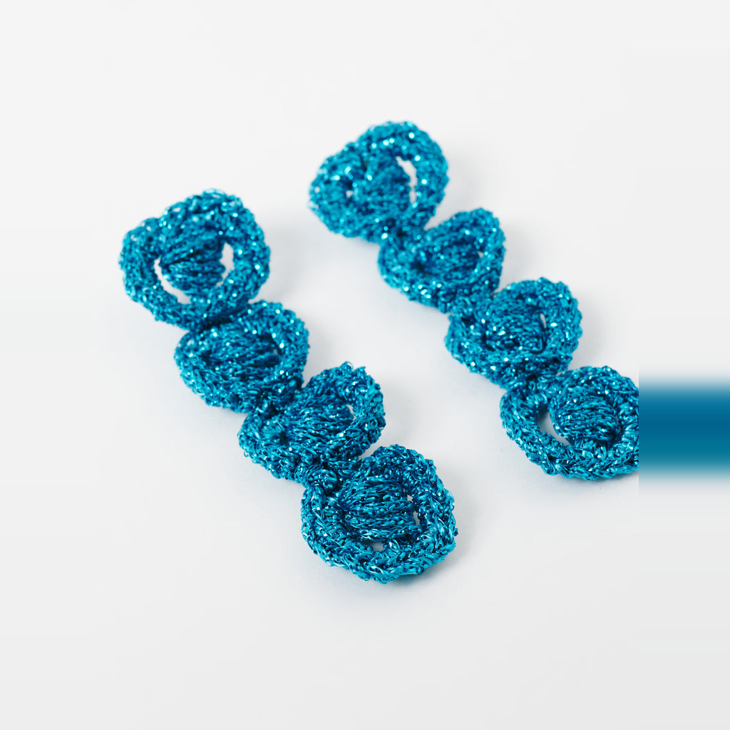 The Arlo long deep teal four-ring crochet loop earrings in an angled flat lay - Lodorfo