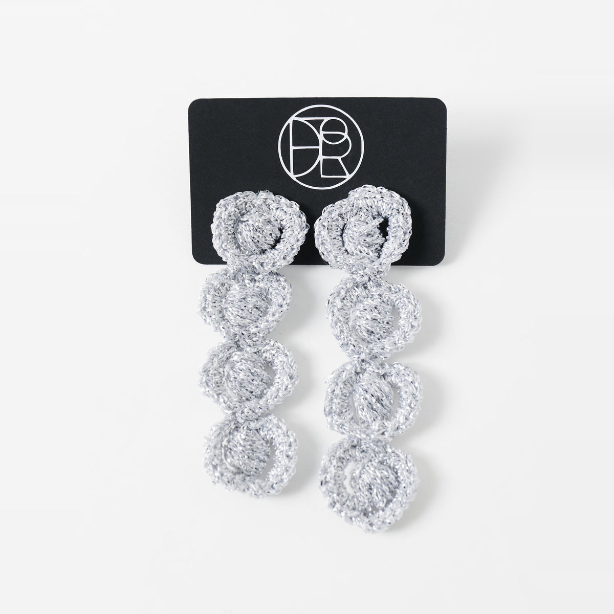 The Arlo long silver grey four-ring crochet loop earrings displayed on a black earring card - Lodorfo