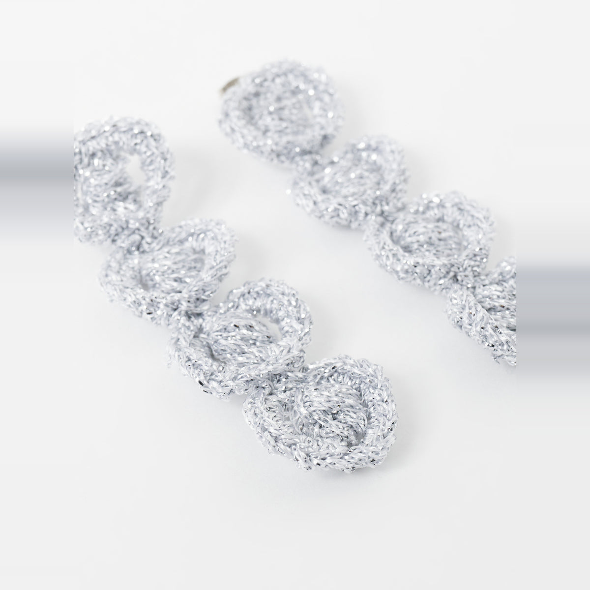 The Arlo long silver grey four-ring crochet loop earrings in an angled flat lay - Lodorfo