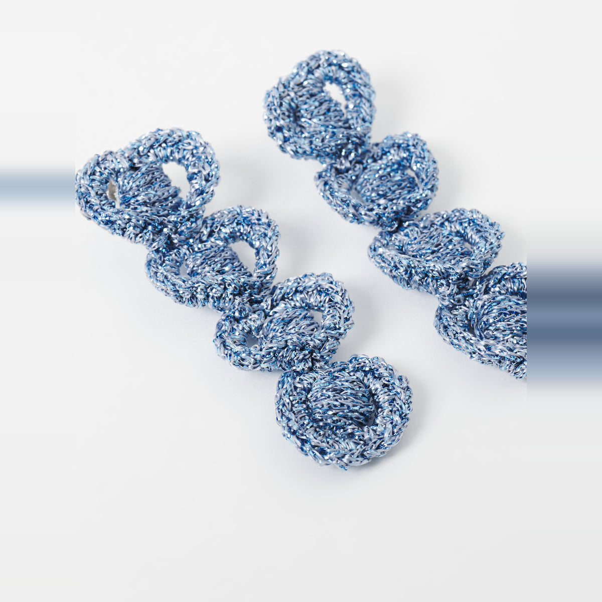The Arlo long sky blue four-ring crochet loop earrings in an angled flat lay - Lodorfo