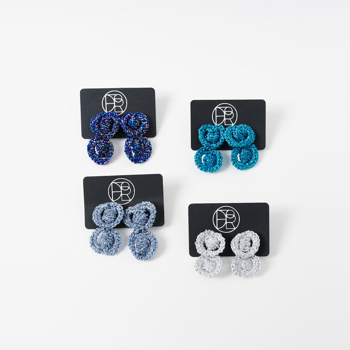 The Arlo short crochet loop earrings in indigo blue, deep teal, silver grey and sky blue on black earring cards - Lodorfo