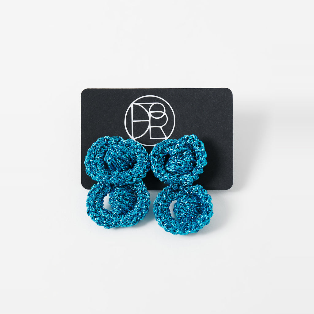 The Arlo short deep teal two-ring crochet loop earrings displayed on a black earring card - Lodorfo