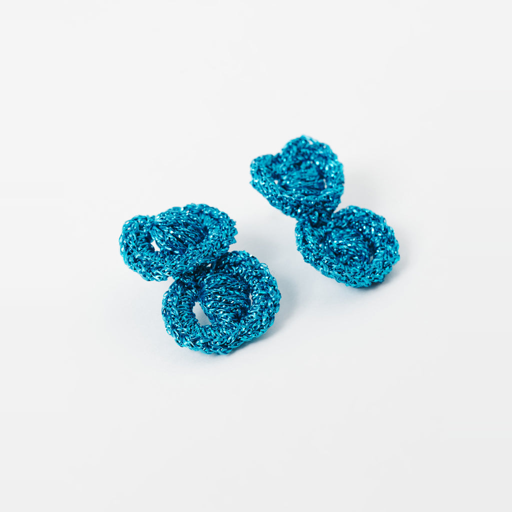 The Arlo short deep teal two-ring crochet loop earrings in an angled flat lay - Lodorfo