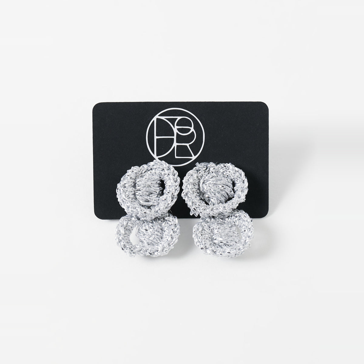 The Arlo short silver grey two-ring crochet loop earrings displayed on a black earring card - Lodorfo