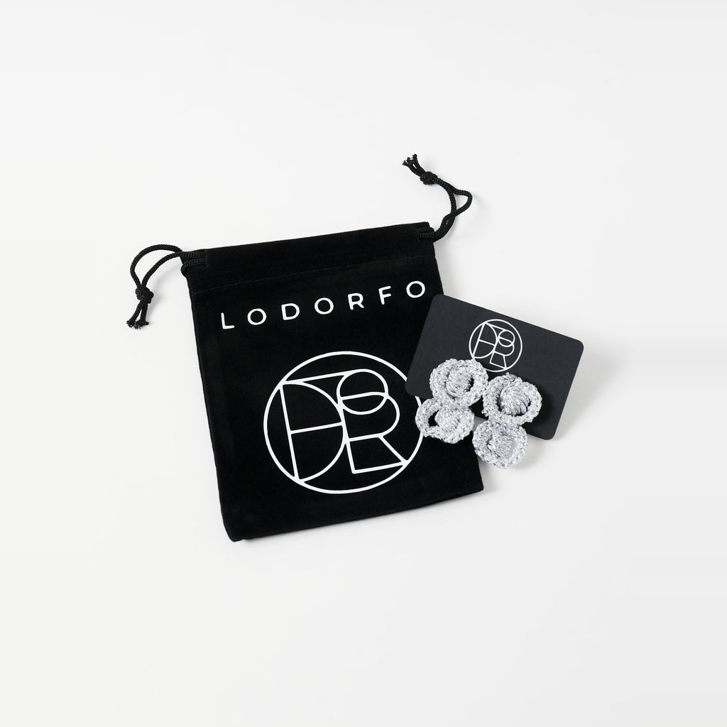 The Arlo short silver grey two-ring crochet loop earrings on a black earring card beside the black velvet gift pouch - Lodorfo