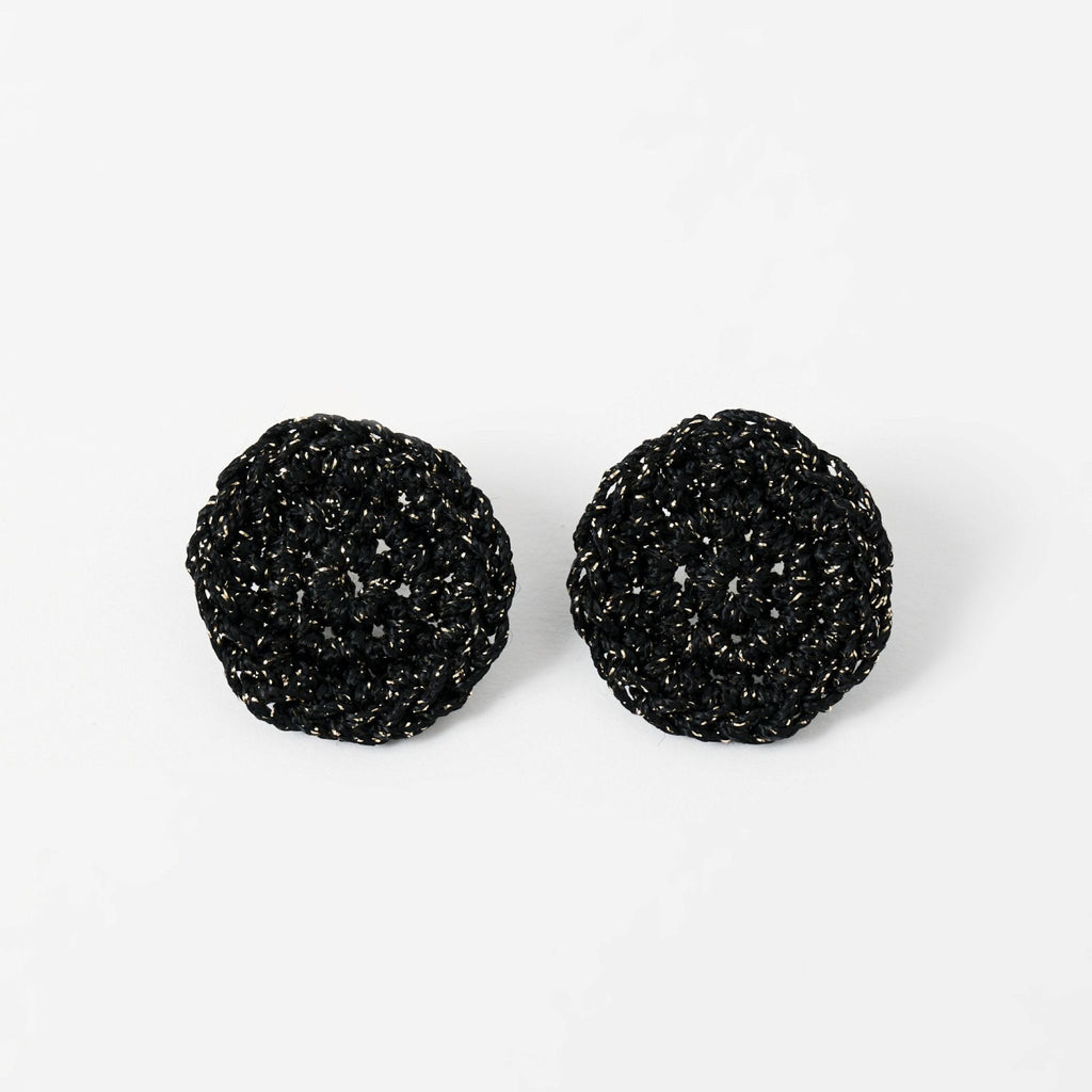 The Vela crochet disc earrings in midnight black with gold shimmer, flat lay - Lodorfo