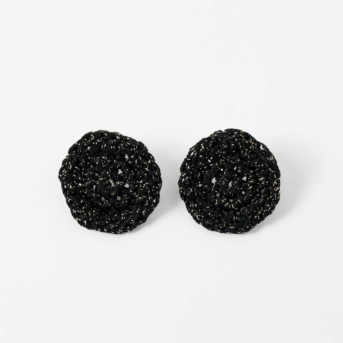 The Vela crochet disc earrings in midnight black with gold shimmer, flat lay - Lodorfo