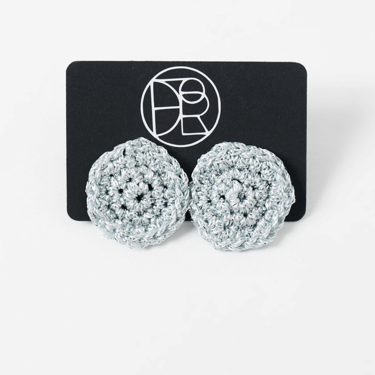The Vela crochet disc earrings in pebble grey with silver shimmer, styled display - Lodorfo