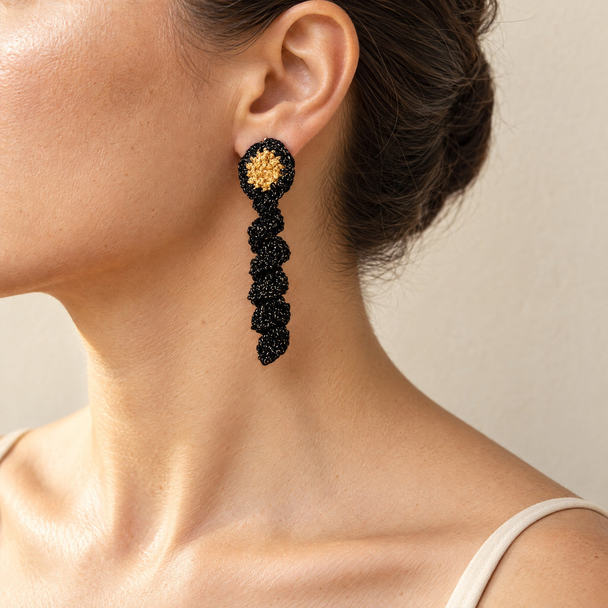 Woman wearing the Noire crochet drop earring with antique-gold centre and black gold-sparkle spiral coil, handmade UK - Lodorfo