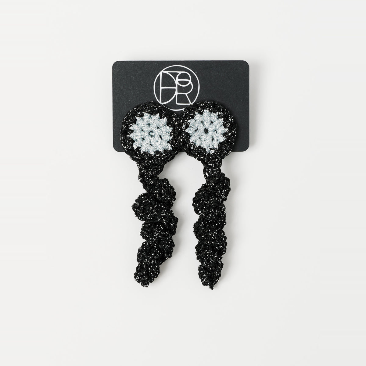 The Noire crochet drop earrings with a silver-grey centre, on a Lodorfo presentation card - Lodorfo