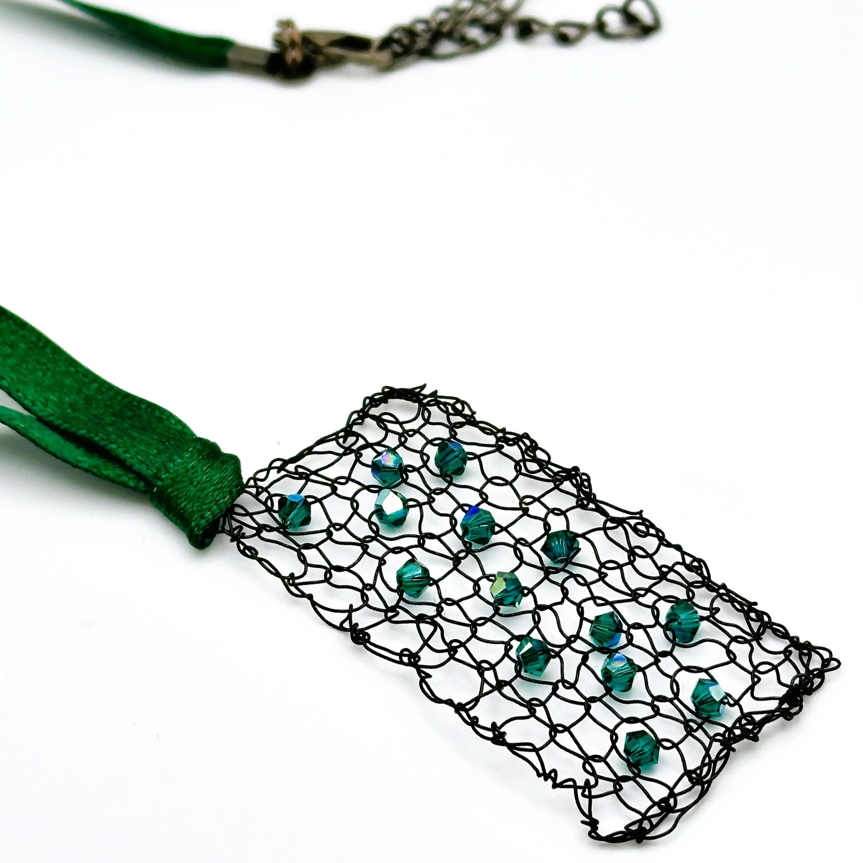 Close-up angled view of the emerald crystal wire mesh pendant and green ribbon, highlighting the intricately woven black wire and sparkling green beads.