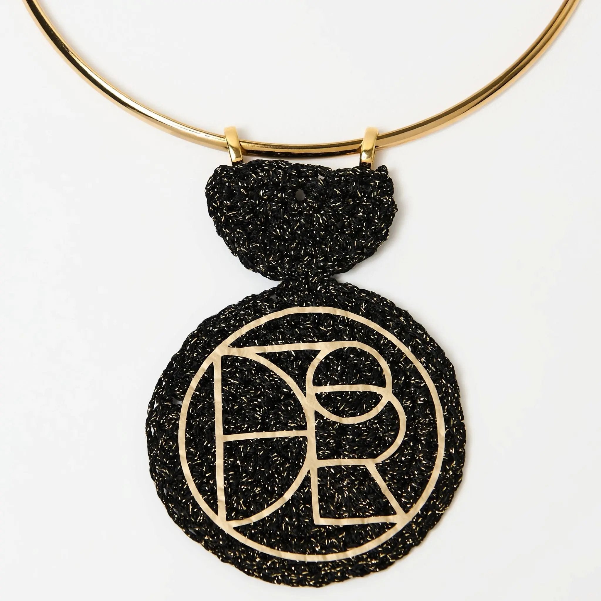 Close-up of circular pendant with abstract geometric gold detailing on a black woven base, hanging from a minimalist gold collar necklace.