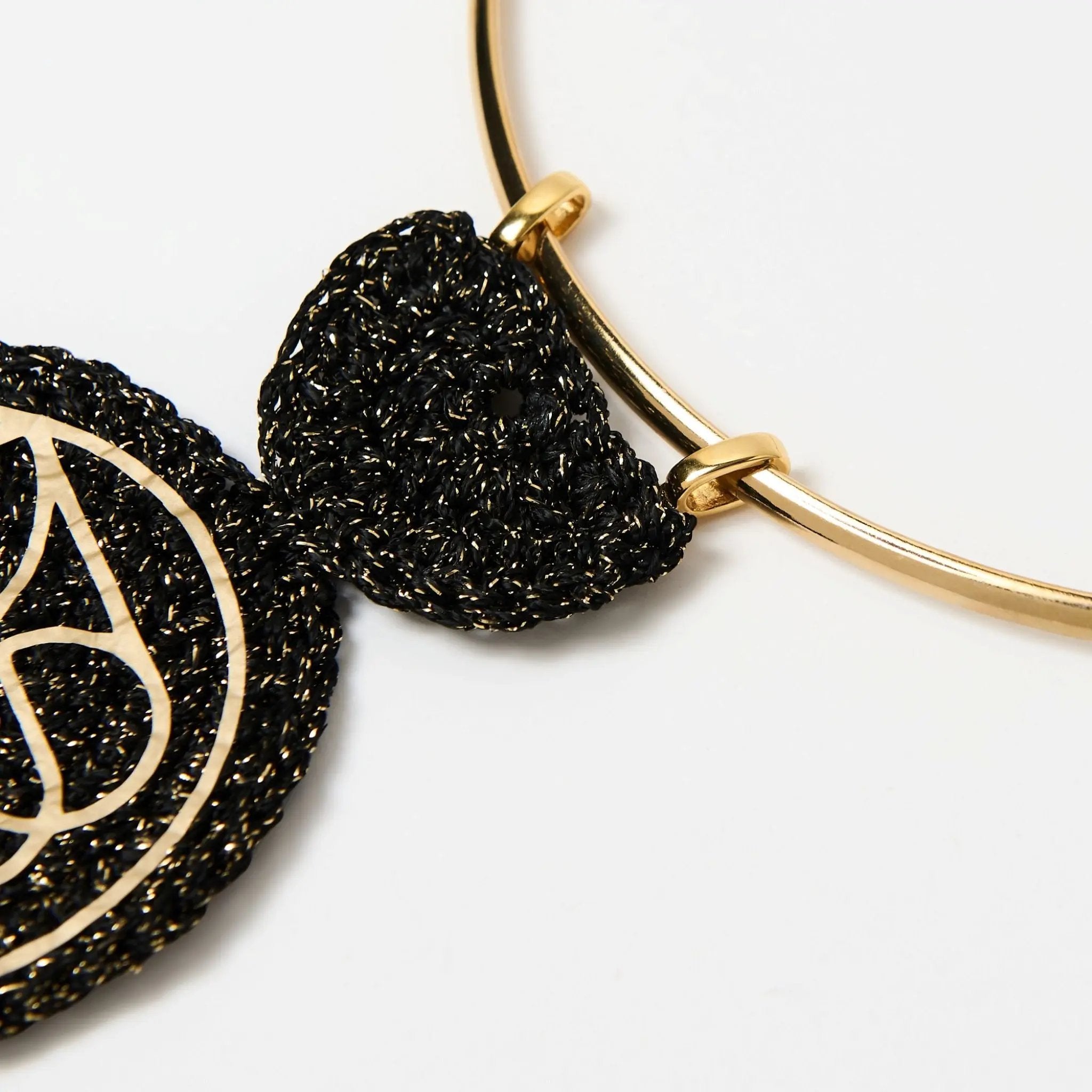 Zoomed-in view showing the intricate attachment of the black textured pendant to the gold collar using dual gold loops.