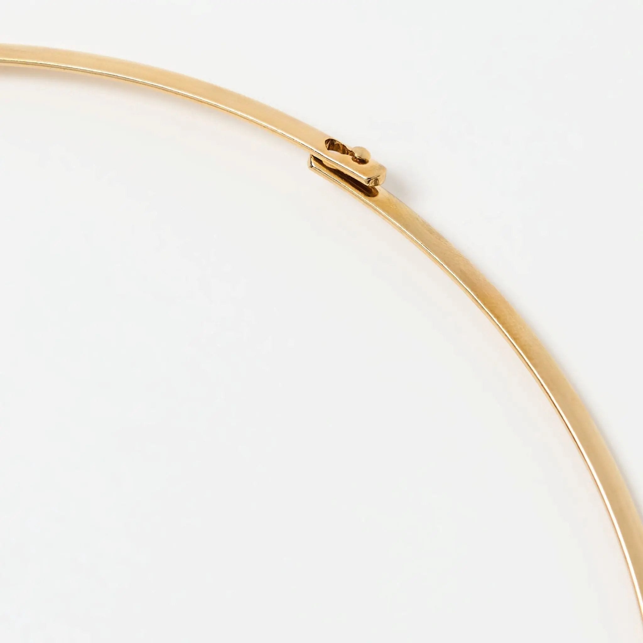 Detail of the gold collar necklace clasp, highlighting its smooth metallic finish and secure closure mechanism.