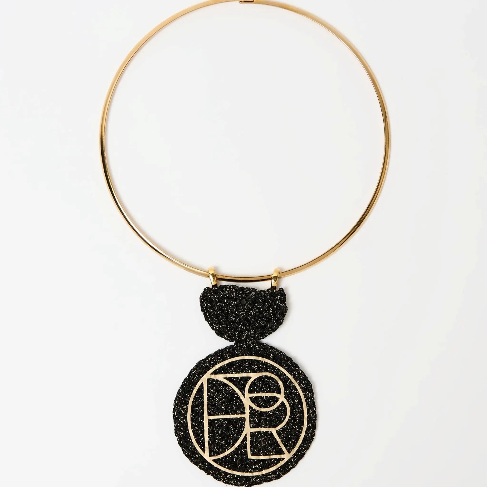 Statement geometric pendant necklace featuring a bold black and gold textured medallion suspended from a sleek gold choker.